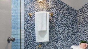 Une salle de bain avec un mur recouvert de carreaux à motifs, des toilettes blanches, une douche en verre et un porte-serviettes.