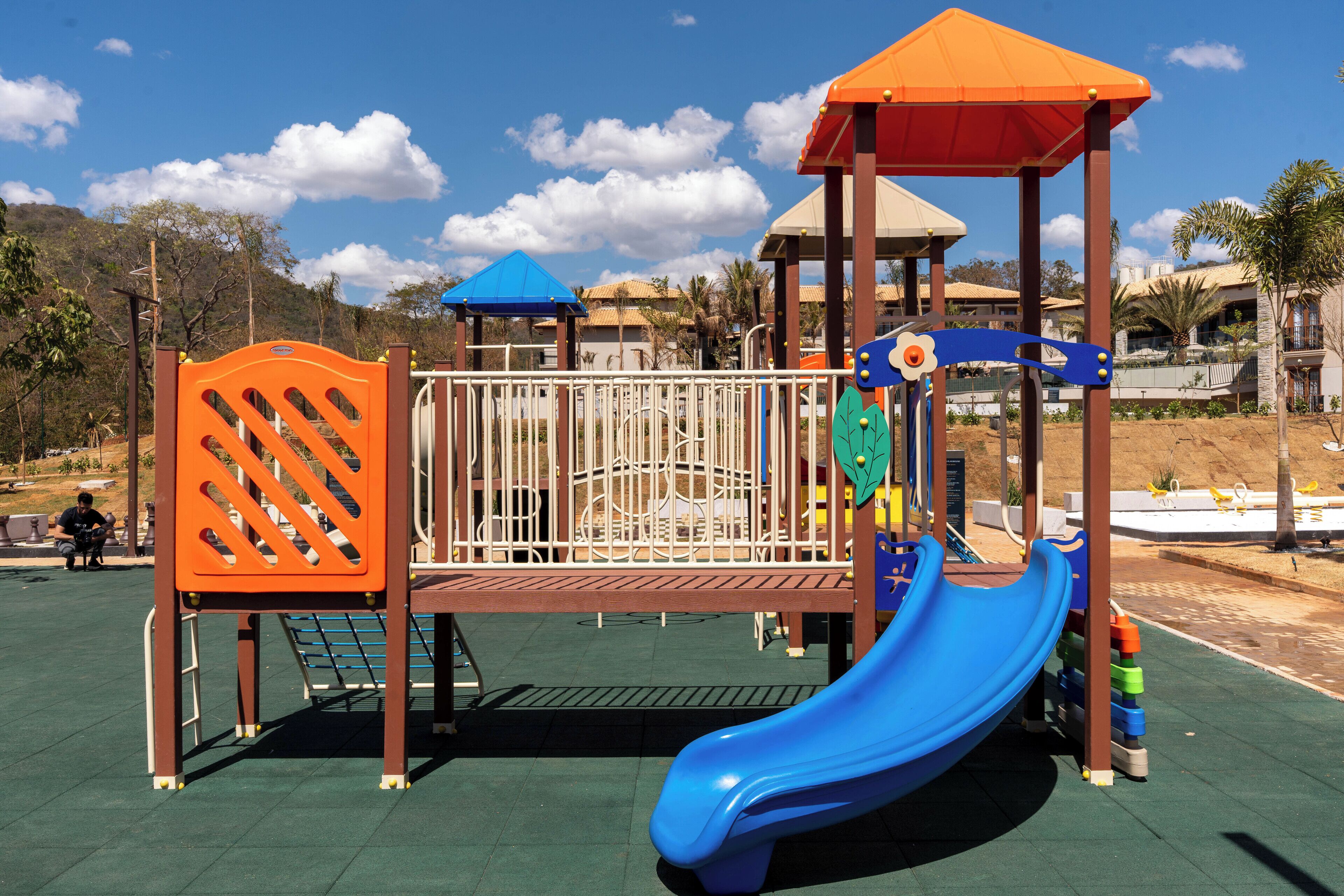Un parque infantil con un tobogán azul, estructuras de escalada naranja y azul, y una zona de juegos cubierta.