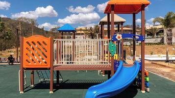 Un parque infantil con un tobogán azul, estructuras de escalada naranja y azul, y una zona de juegos cubierta.