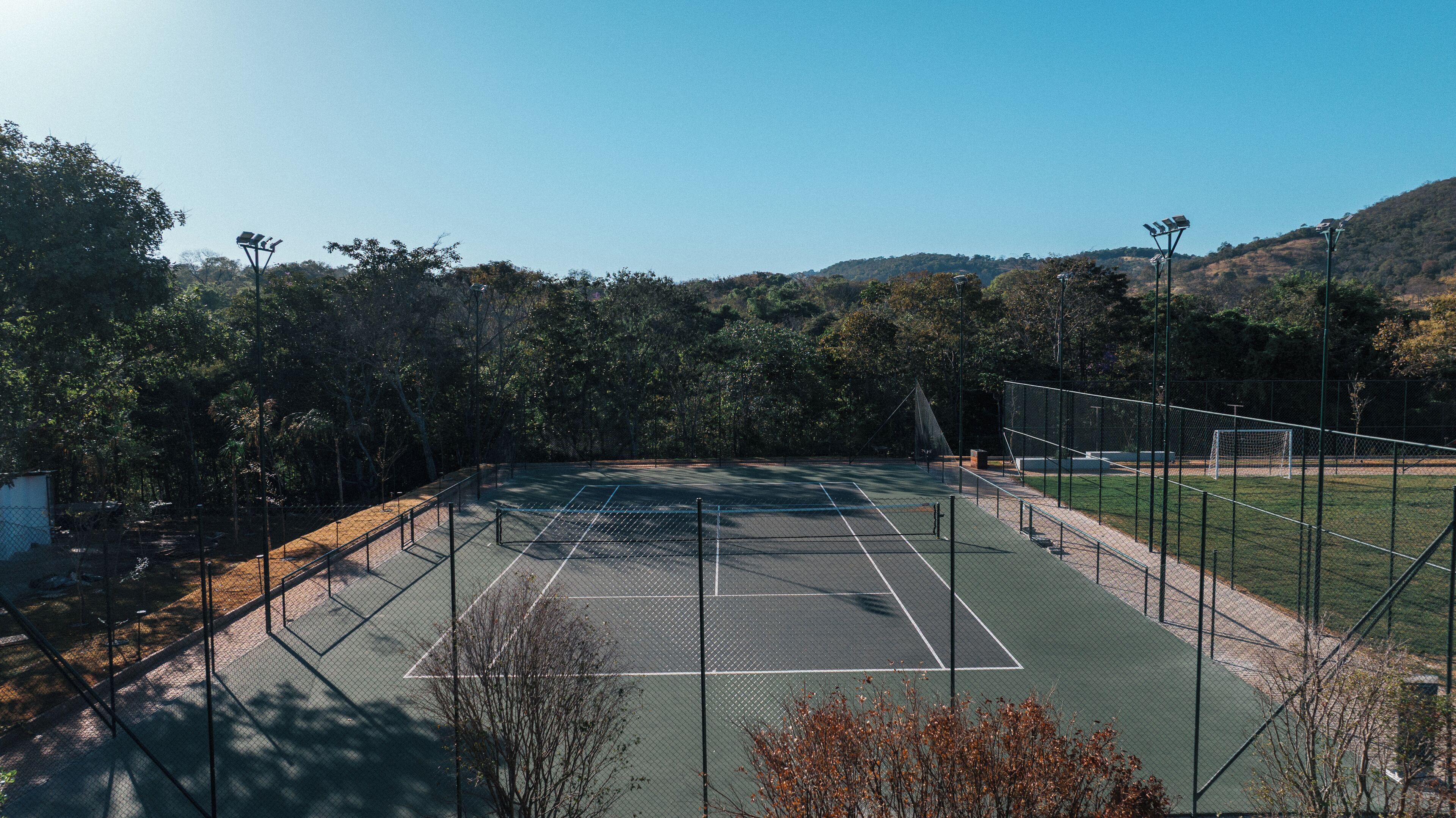 An outdoor tennis court surrounded by trees and hills.