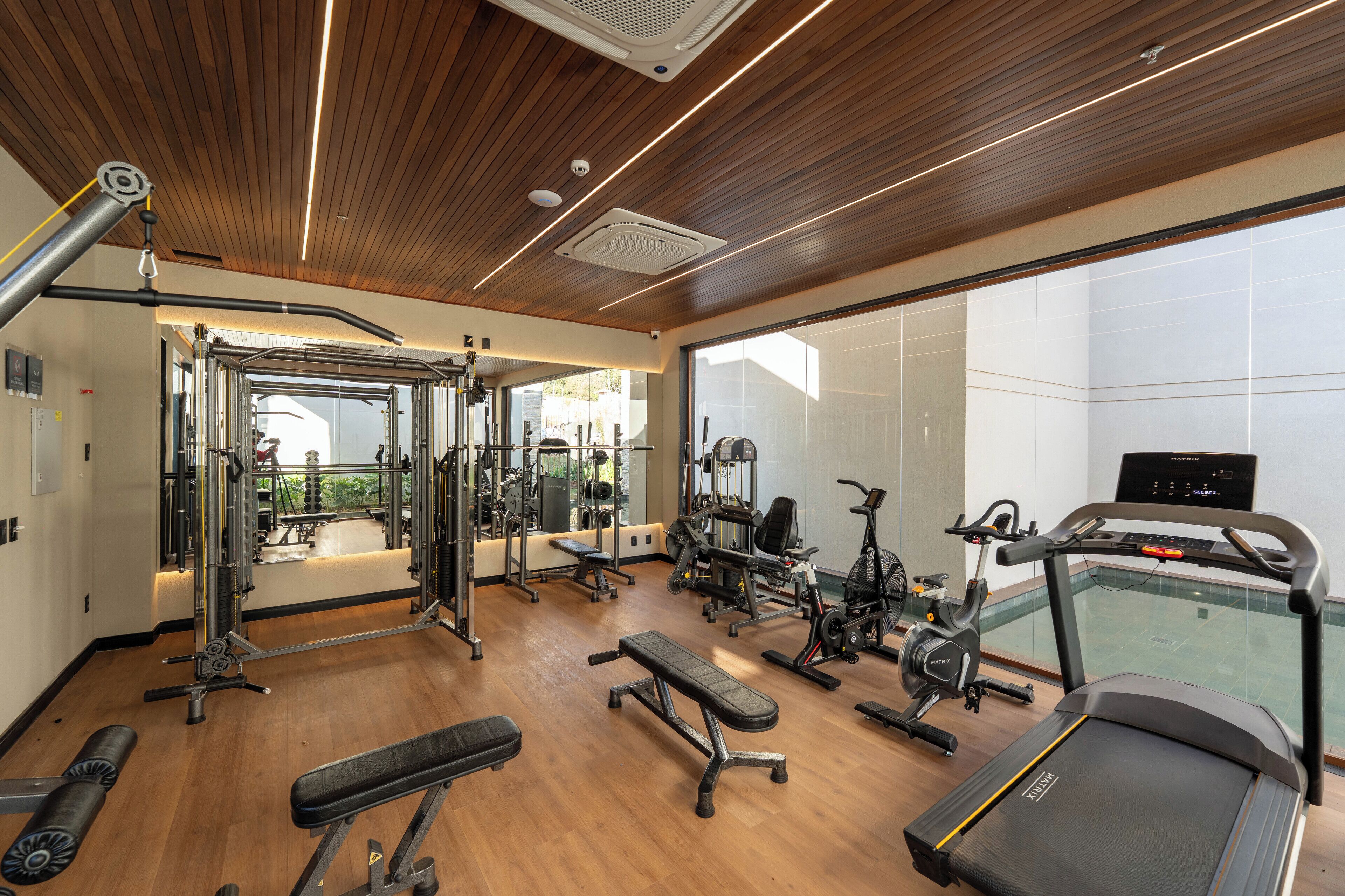 A modern gym with various exercise equipment, a treadmill, and a large window offering a view of the outdoors.