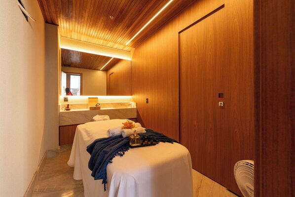 Habitación de hotel con techo de madera, una cama con cubrecama blanco, una pequeña mesa con lámpara y un armario de madera.