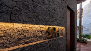 Een spa bordje op een stenen muur, met een houten deur en een houten terras.