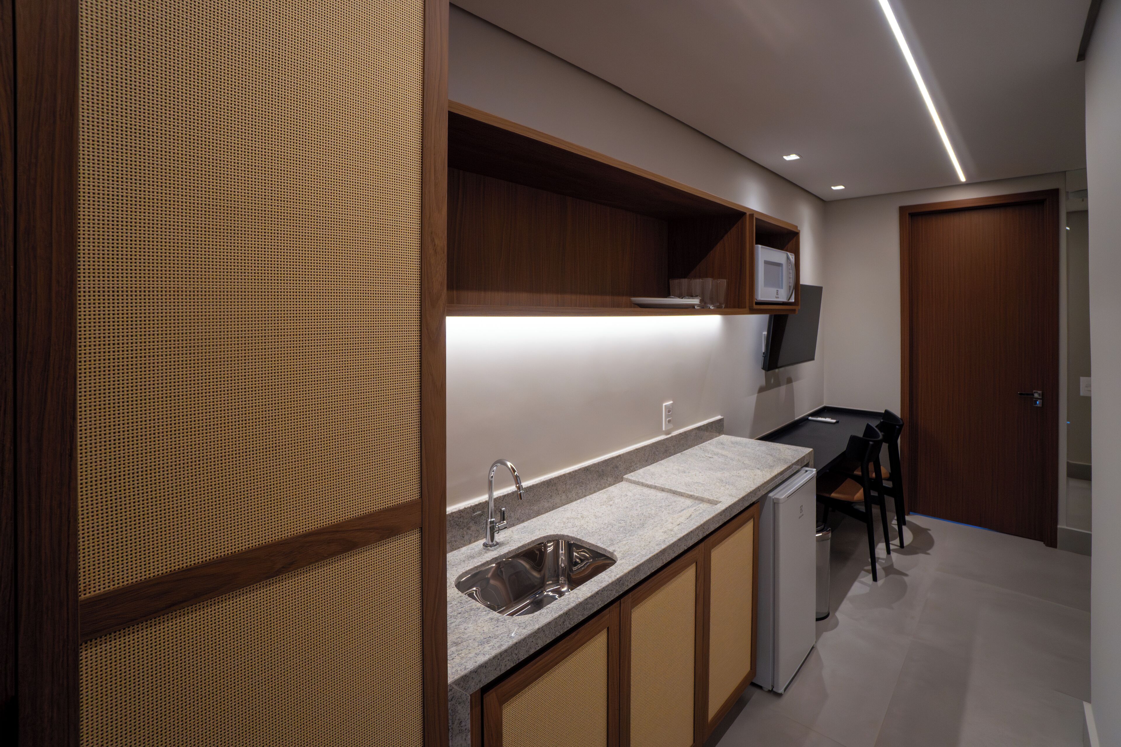 Une cuisine moderne dotée d’un plan de travail en granit, d’un évier en acier inoxydable, de meubles en bois et d’un four à micro-ondes encastré.