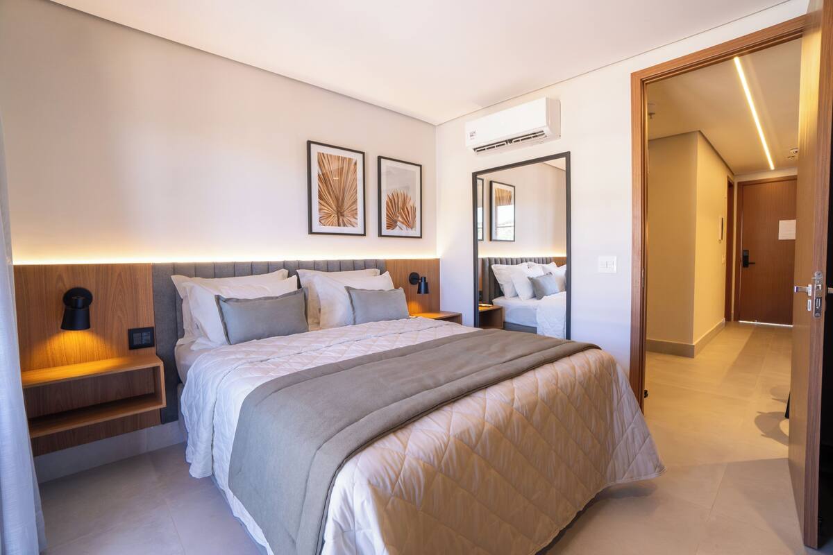 Une chambre moderne avec un grand lit, des tables de chevet, un miroir et des œuvres d’art accrochées au mur.
