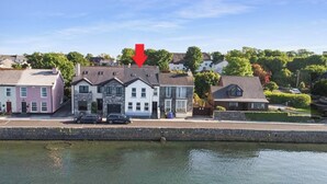 Et hotel ved vandet med en stenfasadde, flere vinduer og en rød pil, der peger mod indgangen.