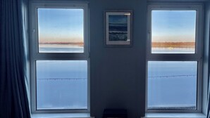 Et værelse med to store vinduer, et billede i ramme på væggen og et lille bord.