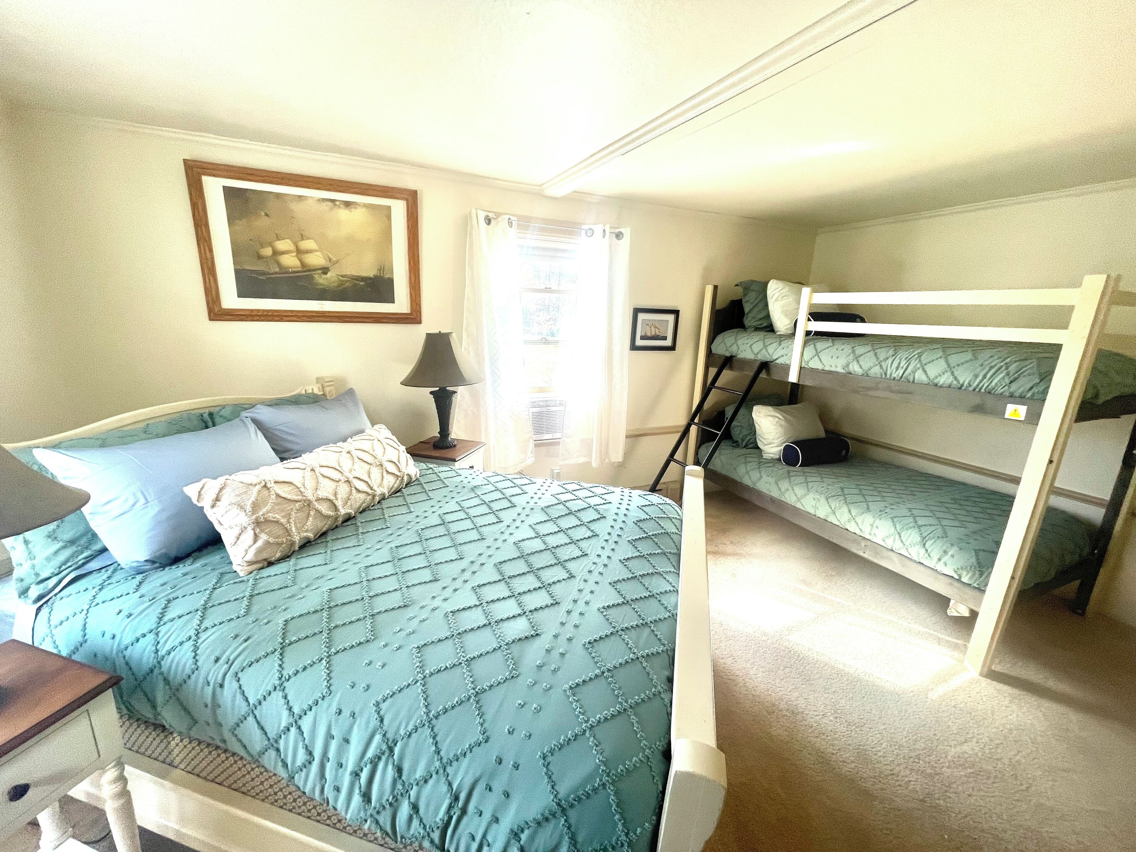 Una habitación con cama, escritorio, lámpara, literas y un cuadro en la pared.