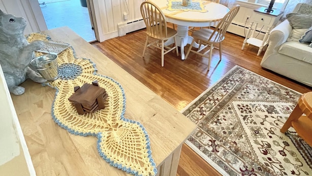 Un comedor con mesa de madera, sillas y una araña. Hay una alfombra en el suelo y un cuadro en la pared.
