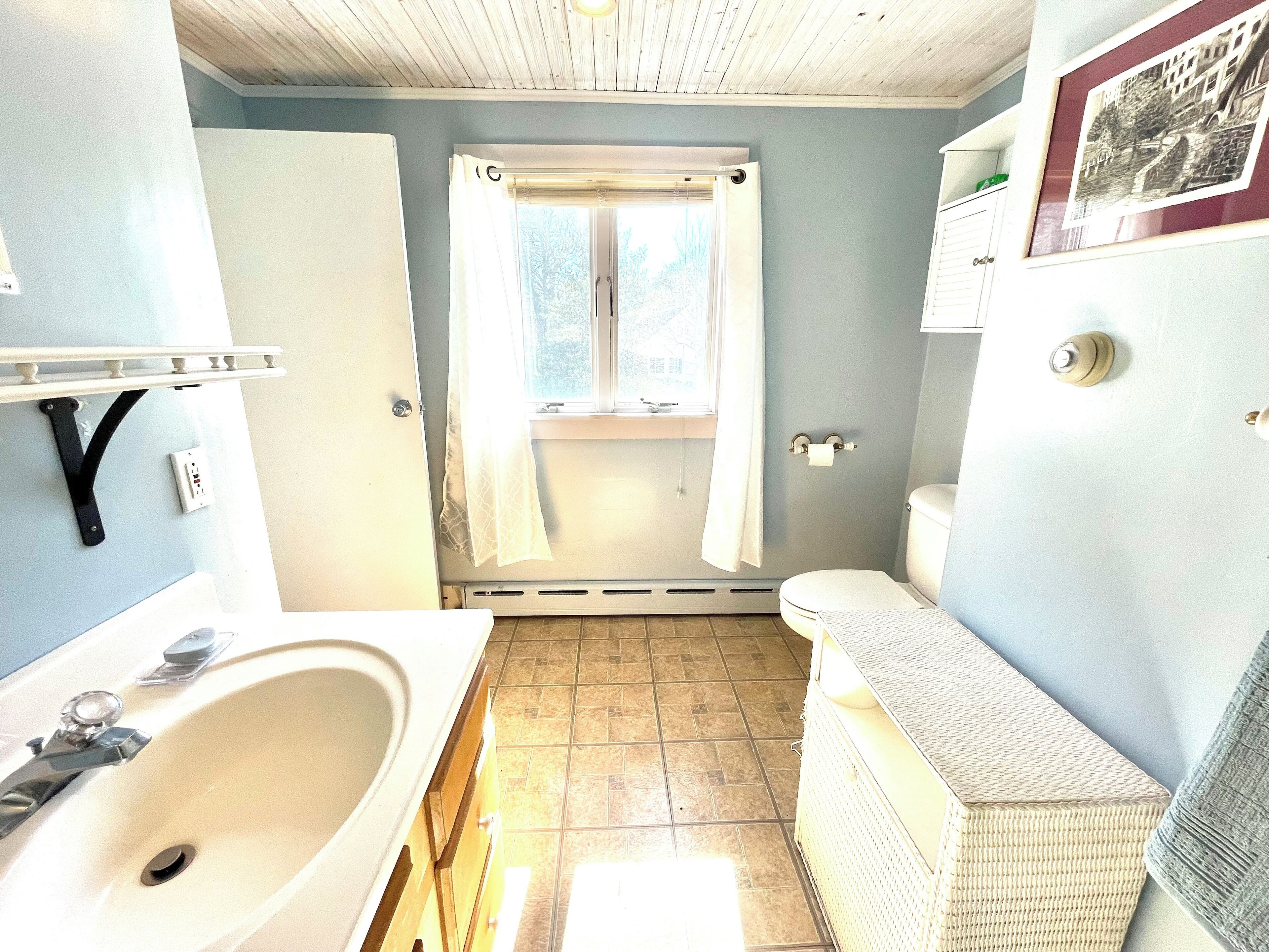 A bathroom with a sink, toilet, and window with a curtain.