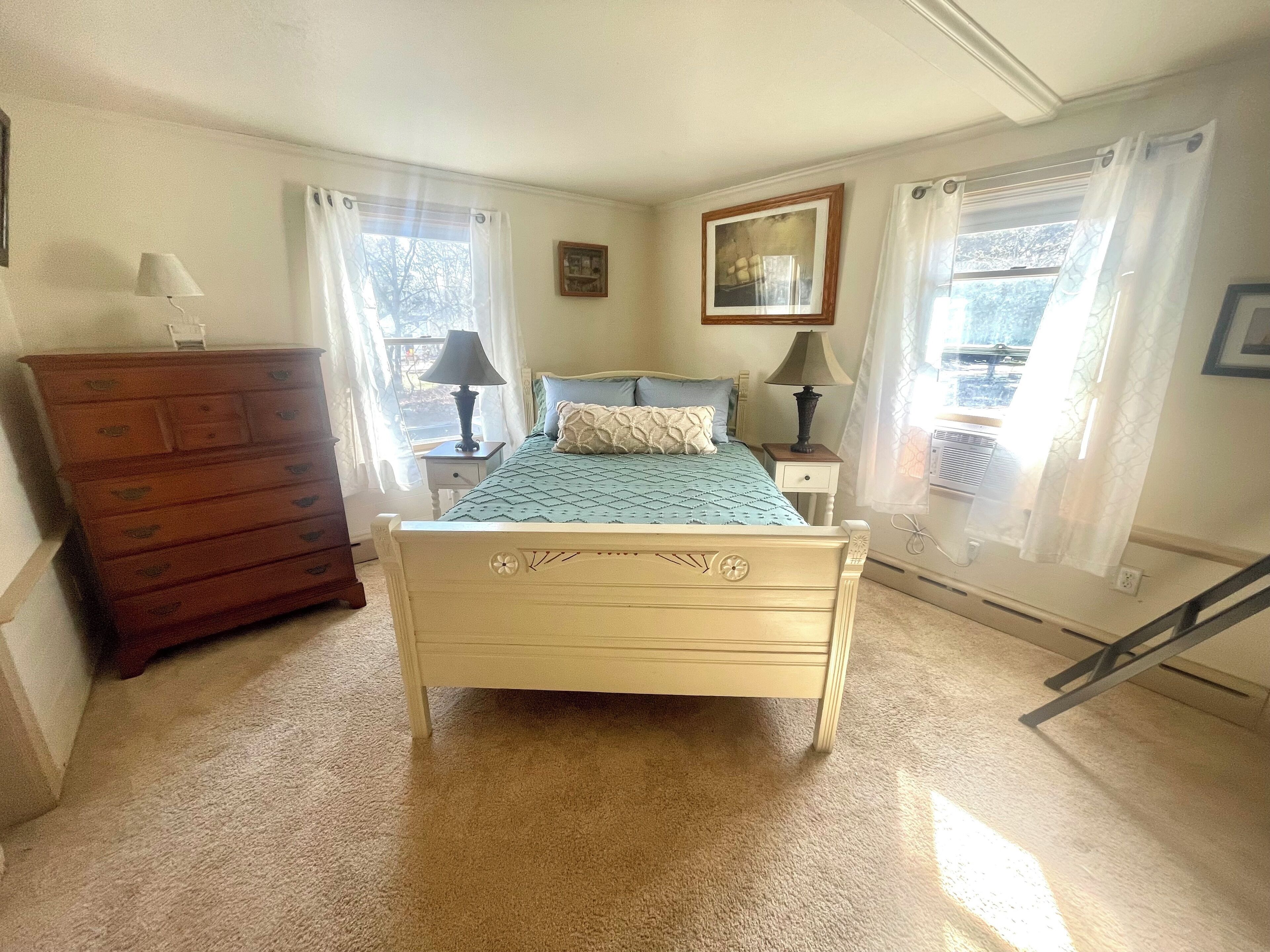 Un dormitorio con cama, dos mesitas de noche, un aparador y una ventana con cortinas.