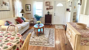 Una sala acogedora con piso de madera, un sofá, una mesa de centro y una mesa de comedor con mantel floreado.