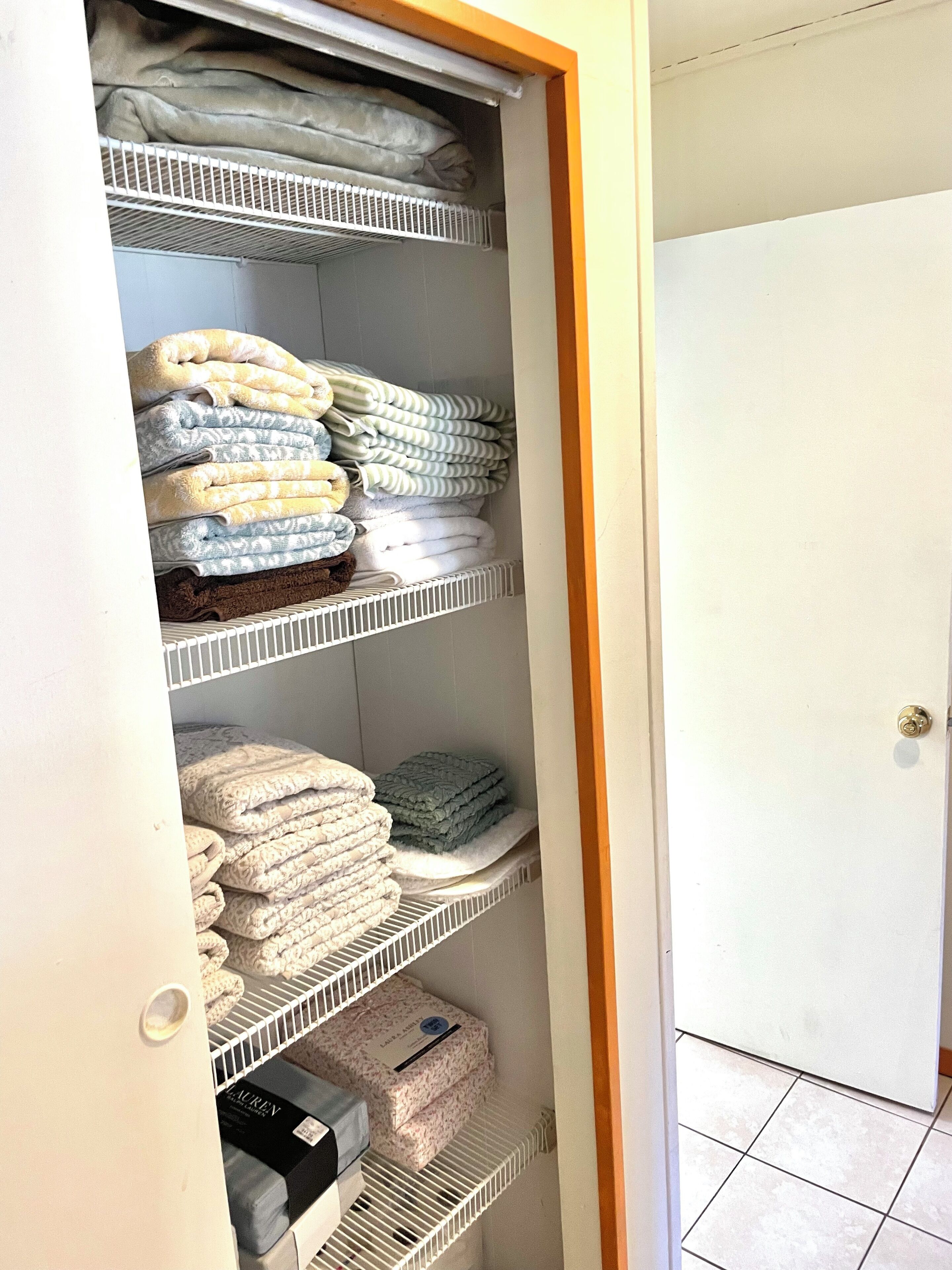 Ein begehbarer Kleiderschrank mit mehreren Regalen voller gefalteter Handtücher und Bettwäsche.