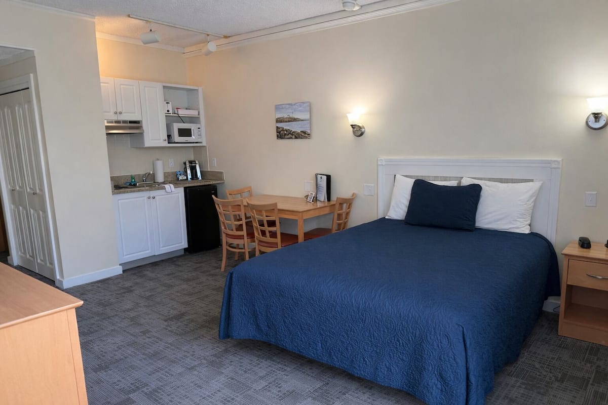 A compact hotel room with a bed, a desk, and a kitchenette.