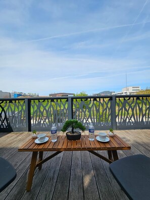 A wooden deck with a table set for two, featuring a bonsai tree centerpiece, two water bottles, and two cups.