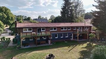 Ein zweistöckiges Gebäude mit rotem Ziegeldach, einer überdachten Terrasse und einem umzäunten Garten.