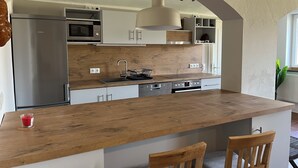 Une cuisine moderne dotée d’un îlot central en bois, d’appareils électroménagers en acier inoxydable et d’un luminaire suspendu.