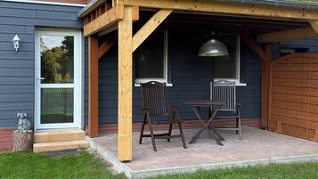 Terraza de madera con mesa y sillas, lámpara colgante y vista de la casa.