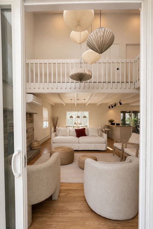 A spacious living area with a high ceiling, a balcony with a railing, and a seating arrangement including a sofa and armchairs.