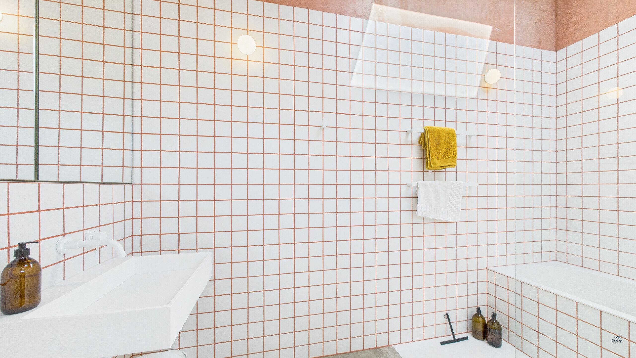 Une salle de bain moderne avec des murs recouverts de carreaux blancs, une baignoire blanche et une serviette jaune suspendue à un porte-serviettes.