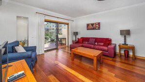A modern living room with a blue sofa, a red sofa, a wooden coffee table, and a large window with a view of buildings.
