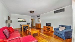 A spacious living room with a red leather sofa, a blue armchair, a wooden coffee table, and a TV stand.