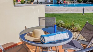 A glass table with a straw hat and a towel, two mesh chairs, and a pool in the background.