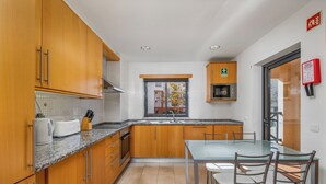 A modern kitchen with wooden cabinets, a granite countertop, and a dining area with a glass table and metal chairs.