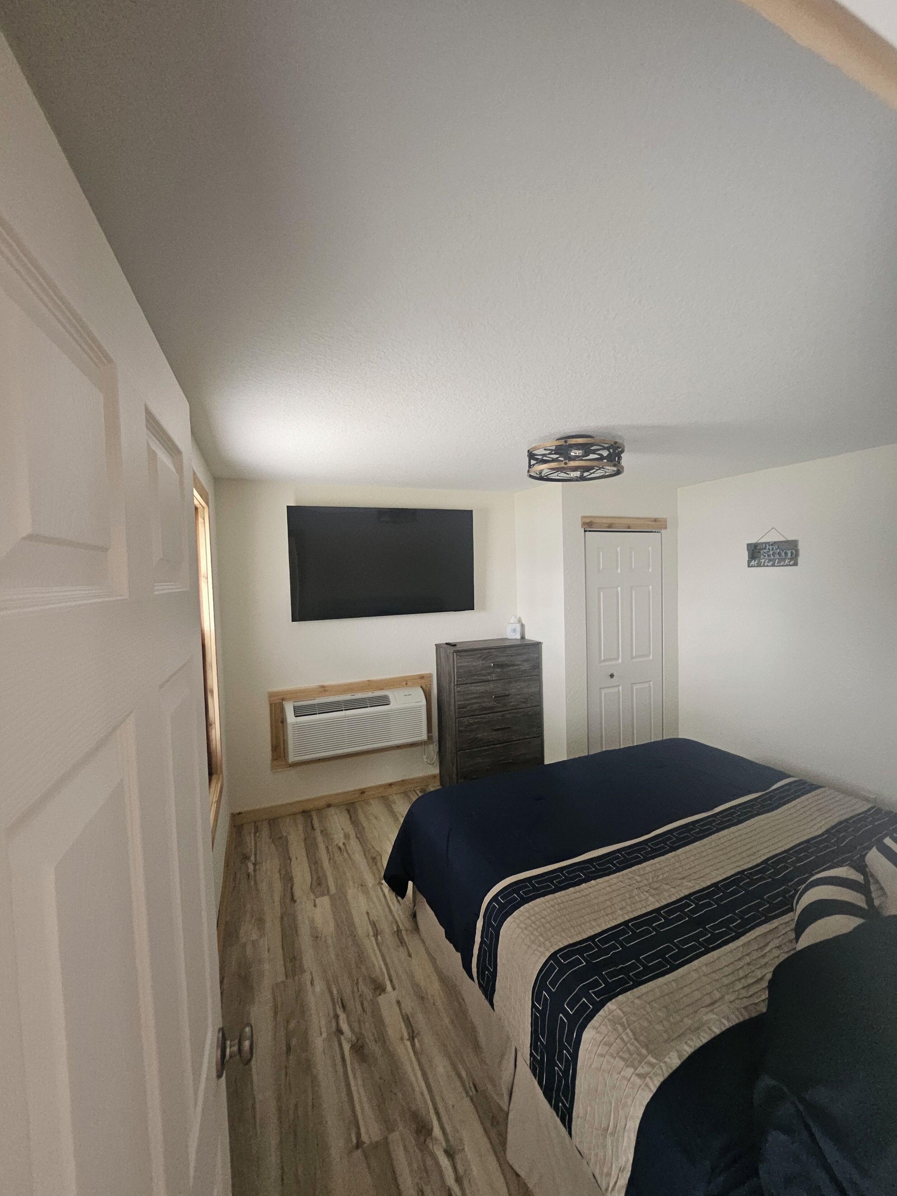 Una camera da letto con un letto, una cassettiera, una TV a parete e una porta.