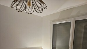 Et soveværelse med sengegavl i træ, et sengelinned med mønster, en sengetavlelampe og et vindue med skodder.
