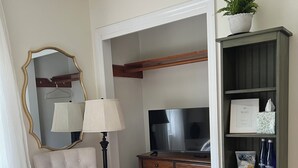 A hotel room with a bed, a chair, a dresser, a TV, a lamp, a mirror, a plant, and a bookshelf.