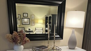 A white dresser with gold handles, a vase of flowers, a mirror, and a lamp.