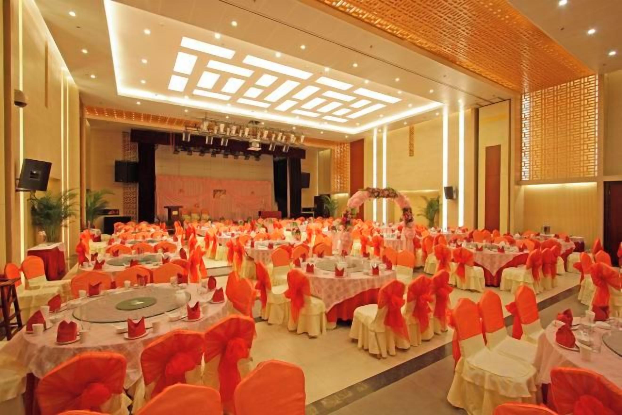 Uma sala de banquetes com mesas redondas e cadeiras, um palco e uma tela grande.