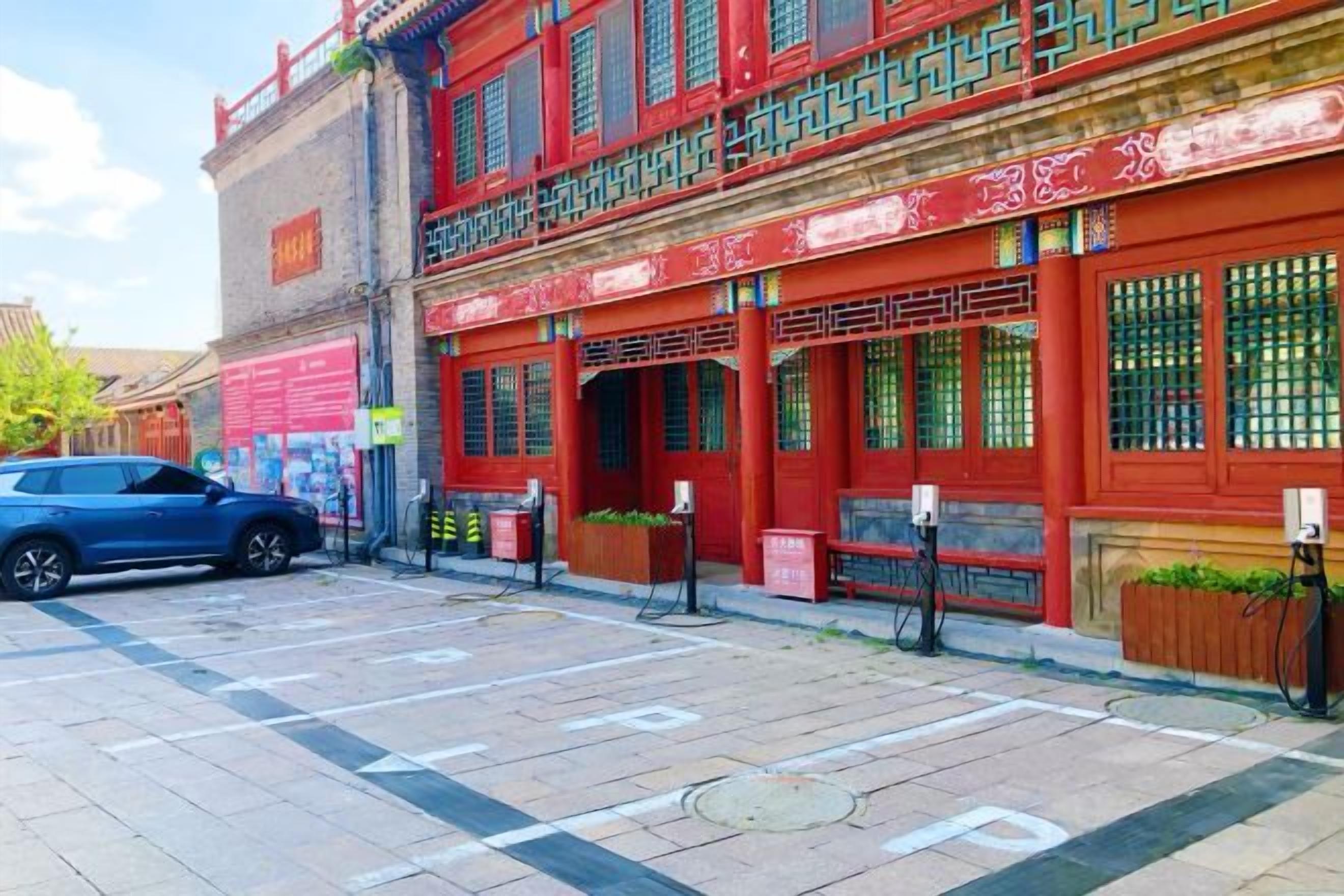 A red building with traditional Chinese architectural elements, a parking lot, and a blue car.