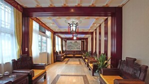 Un vestíbulo de hotel con una larga recepción, zona de estar con sofás y sillones, y un cuadro grande en la pared.