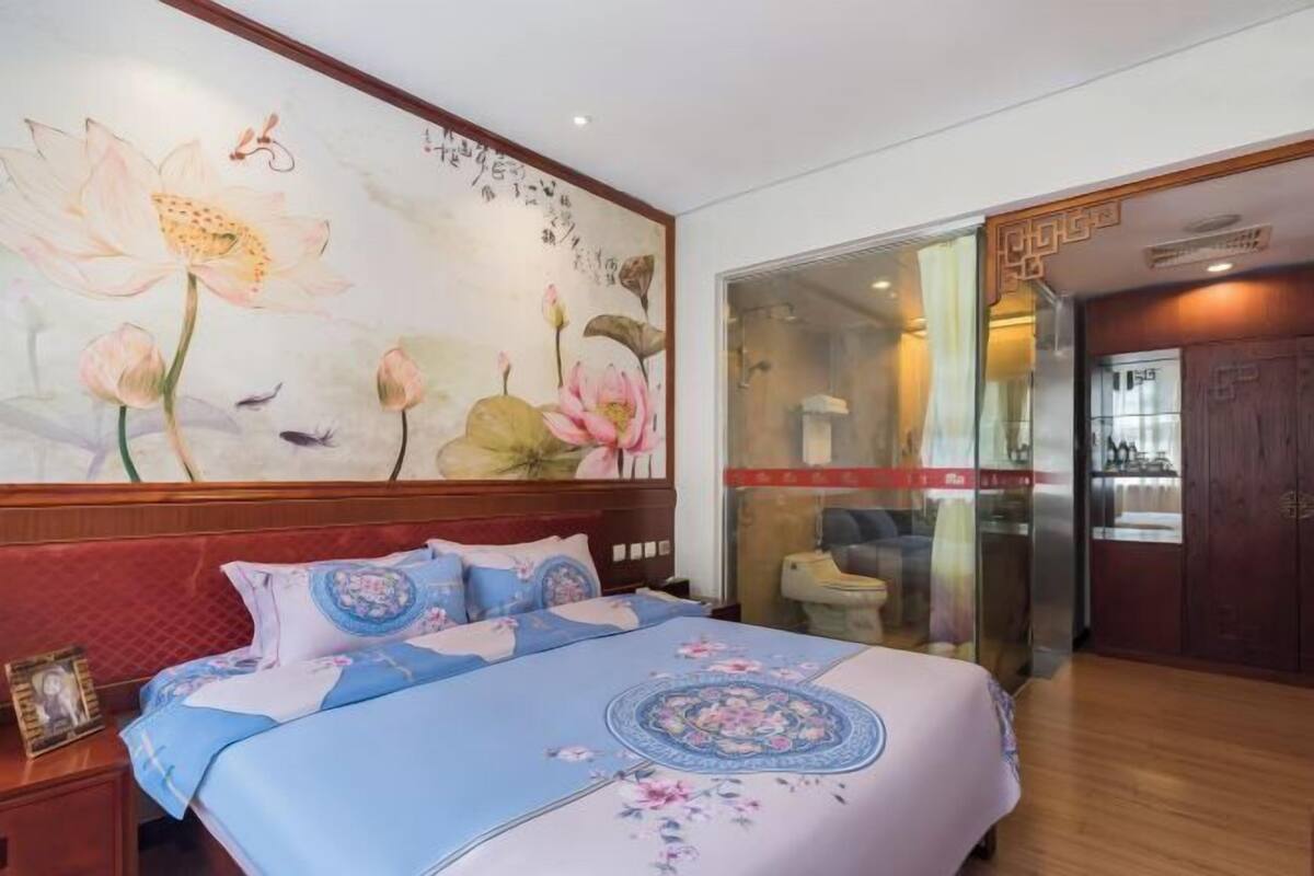 Habitación de hotel con un gran mural floral en la pared, una cama con ropa de cama floral y una puerta corrediza de vidrio que da a un baño.