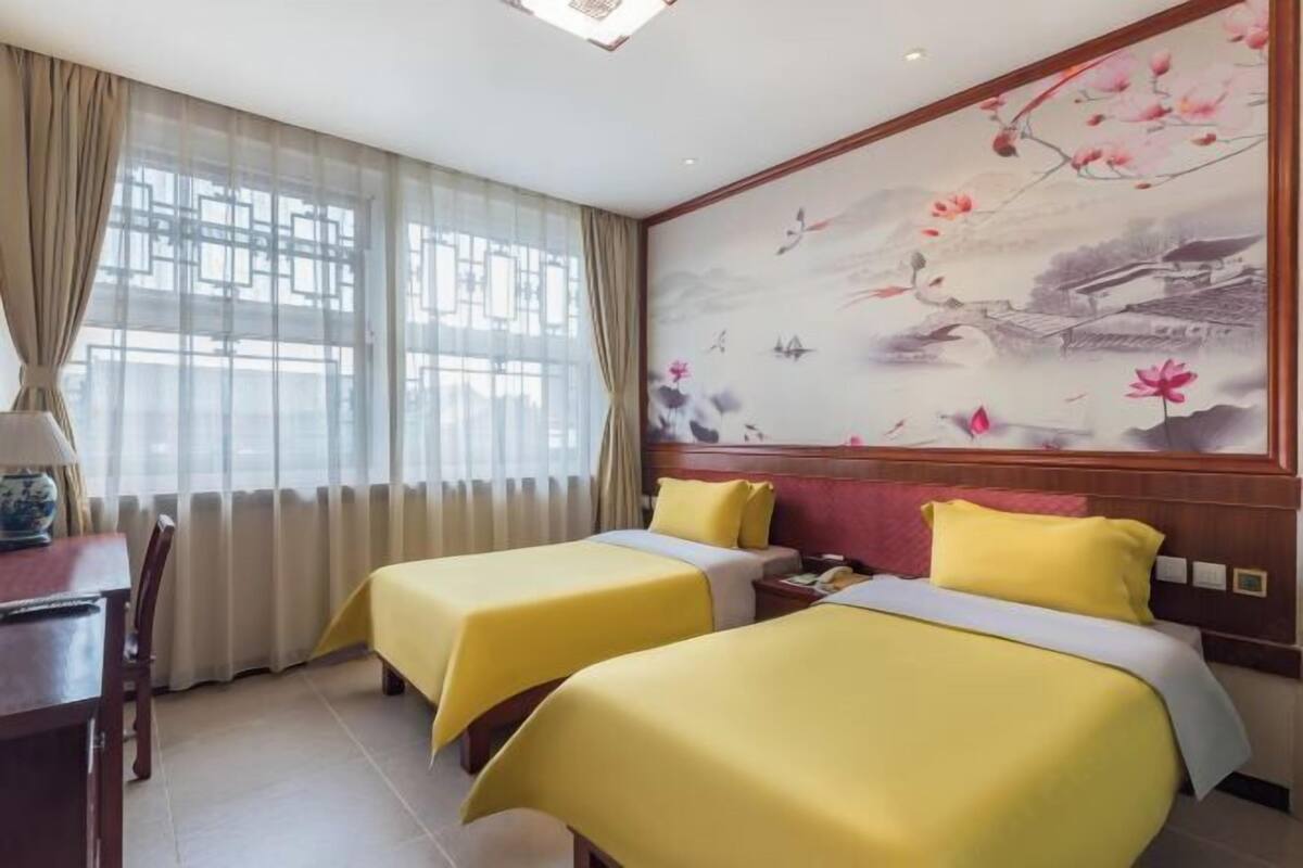 Habitación de hotel con dos camas, un escritorio y un gran mural en la pared.