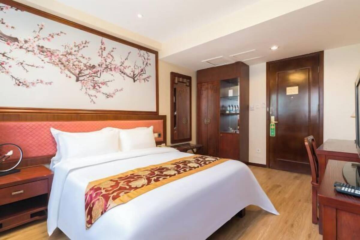 Habitación de hotel con una cama grande, cabecera de madera, escritorio con silla y televisor montado en la pared.