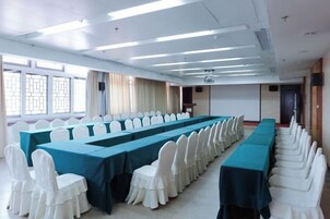 Un salón de conferencias con una larga mesa, filas de sillas y una pantalla de proyector.