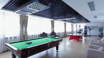 A pool table in a room with large windows, a ceiling fan, and a red exercise machine.