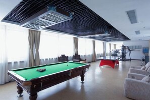 A pool table in a room with large windows, a ceiling fan, and a red exercise machine. - Shanhai Holiday Hotel (Qinhuangdao)