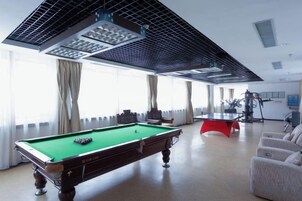 A pool table in a room with large windows, a ceiling fan, and a red exercise machine.