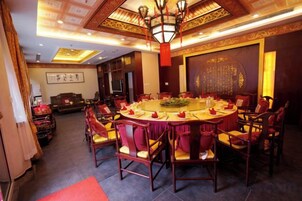 A traditional banquet hall with a round table, red upholstered chairs, and a chandelier.