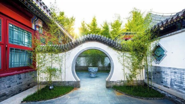 Un patio tradicional chino con un arco de piedra, un edificio rojo y un muro con tejas.