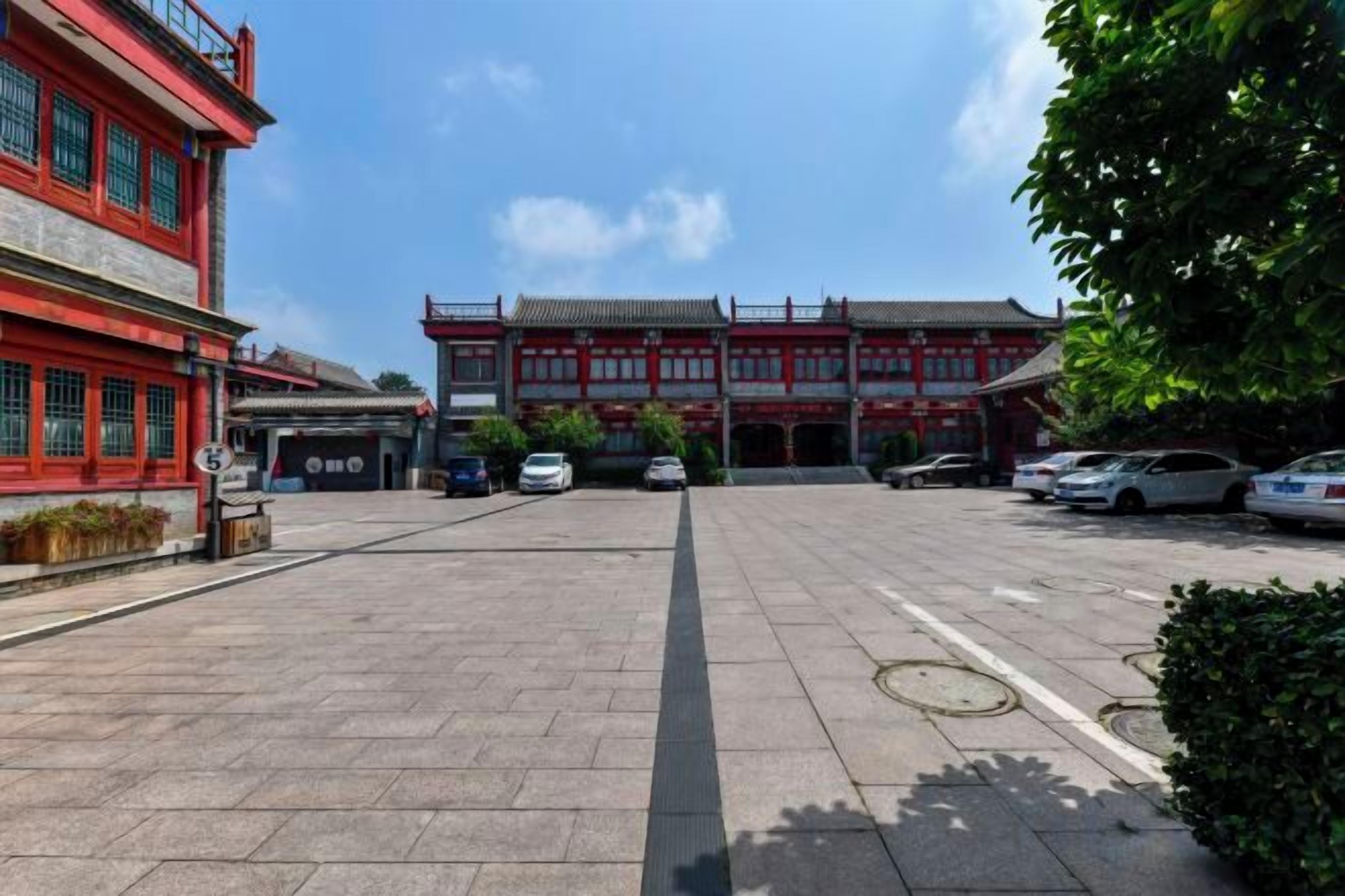 A courtyard with traditional architecture, a parking area, and a clear sky.