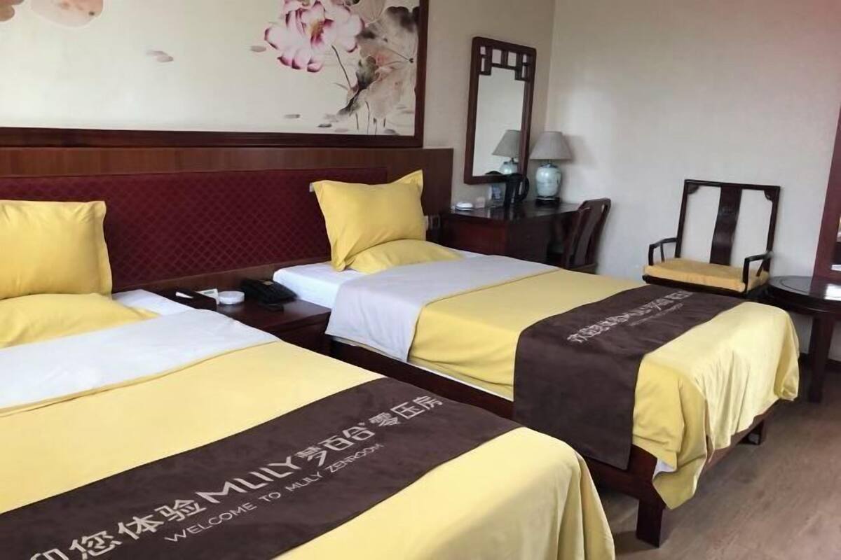 Una habitación de hotel con dos camas, un cabecero de madera, una mesita de noche, una silla, un escritorio, una lámpara y un espejo.