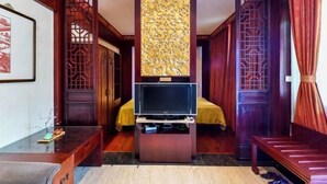 Una habitación tradicional con una televisión sobre un mueble bajo, una cama con colcha amarilla, muebles de madera y paneles decorativos.