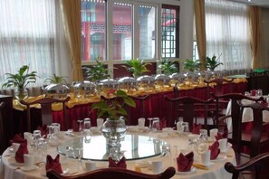 Uma área de refeições com mesas redondas preparadas para vários convidados, com copos e guardanapos dobrados.