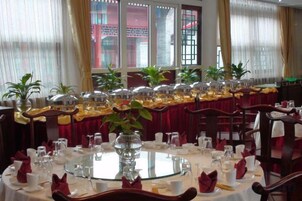 Un comedor con mesas redondas dispuestas para varios invitados, con cristalería y servilletas dobladas.