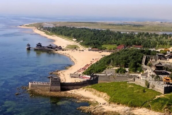 Zona costera con playa, una estructura fortificada y vegetación circundante.
